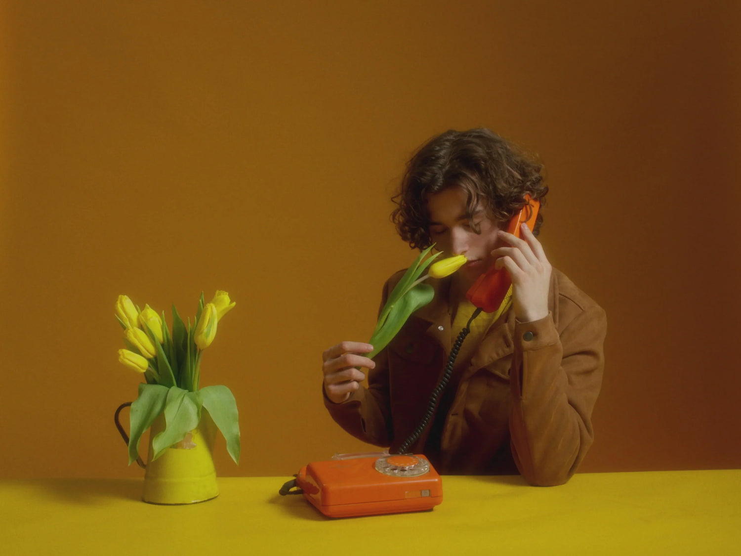 Young man smelling a yellow flower while holding a telephone